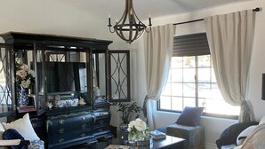 Ein geräumiges Wohnzimmer mit einem dunklen Holzschrank, einem Ledersofa, einem Couchtisch und einer Chandelier.