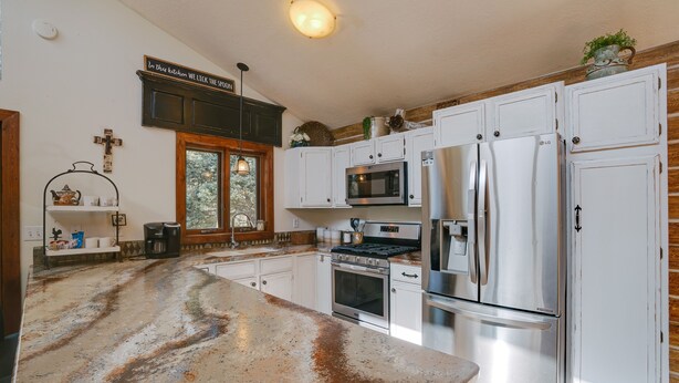 A kitchen with white cabinets, stainless steel appliances, a granite countertop, and a cross on the wall. - Home near Monte Verde Lake with forest views (Angel Fire)