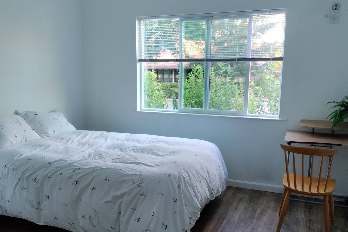 A bedroom with a bed, a window, a chair, and a small table.