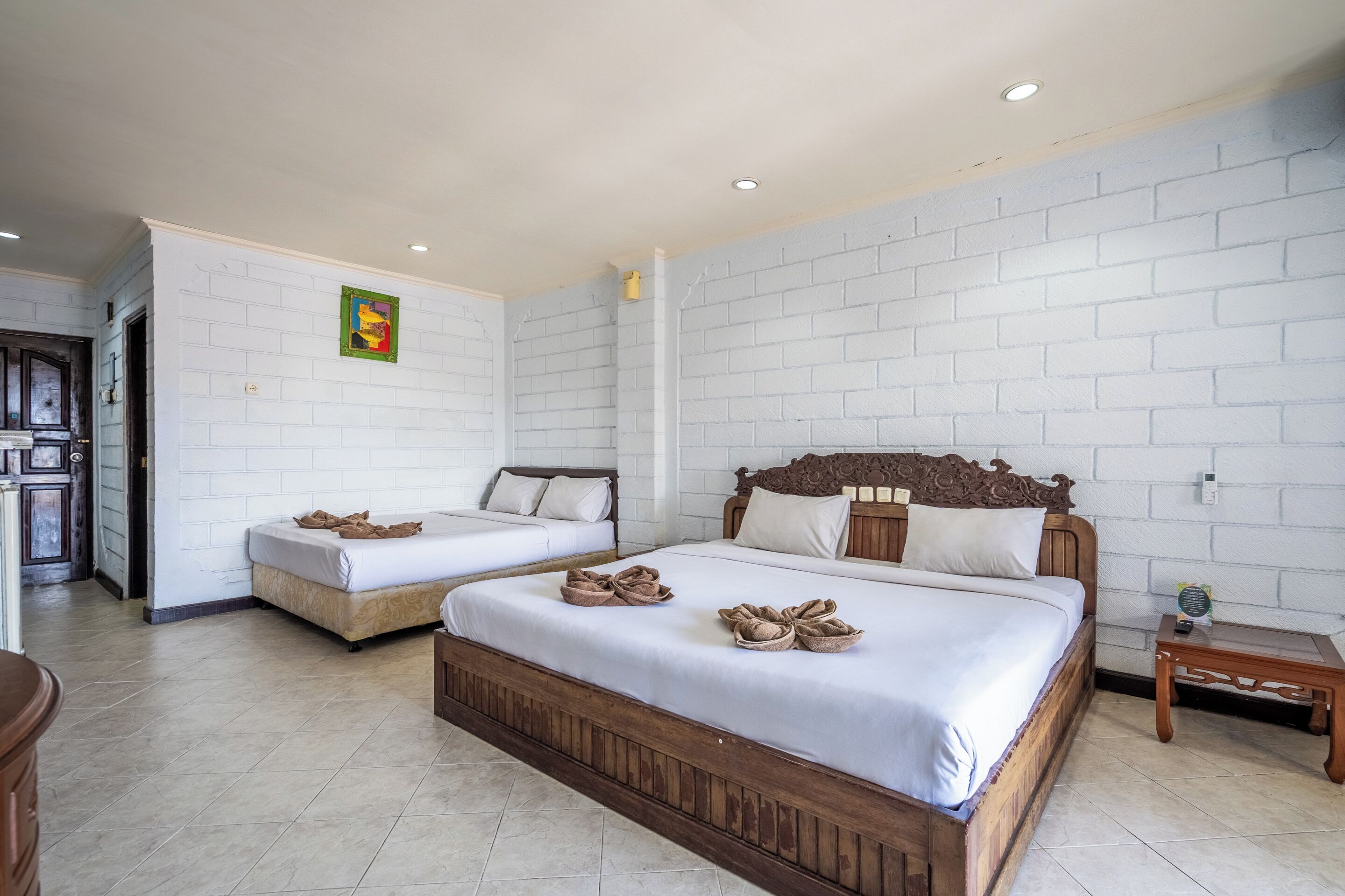 Habitación de hotel con dos camas, paredes de ladrillo blanco y cabecero de madera.