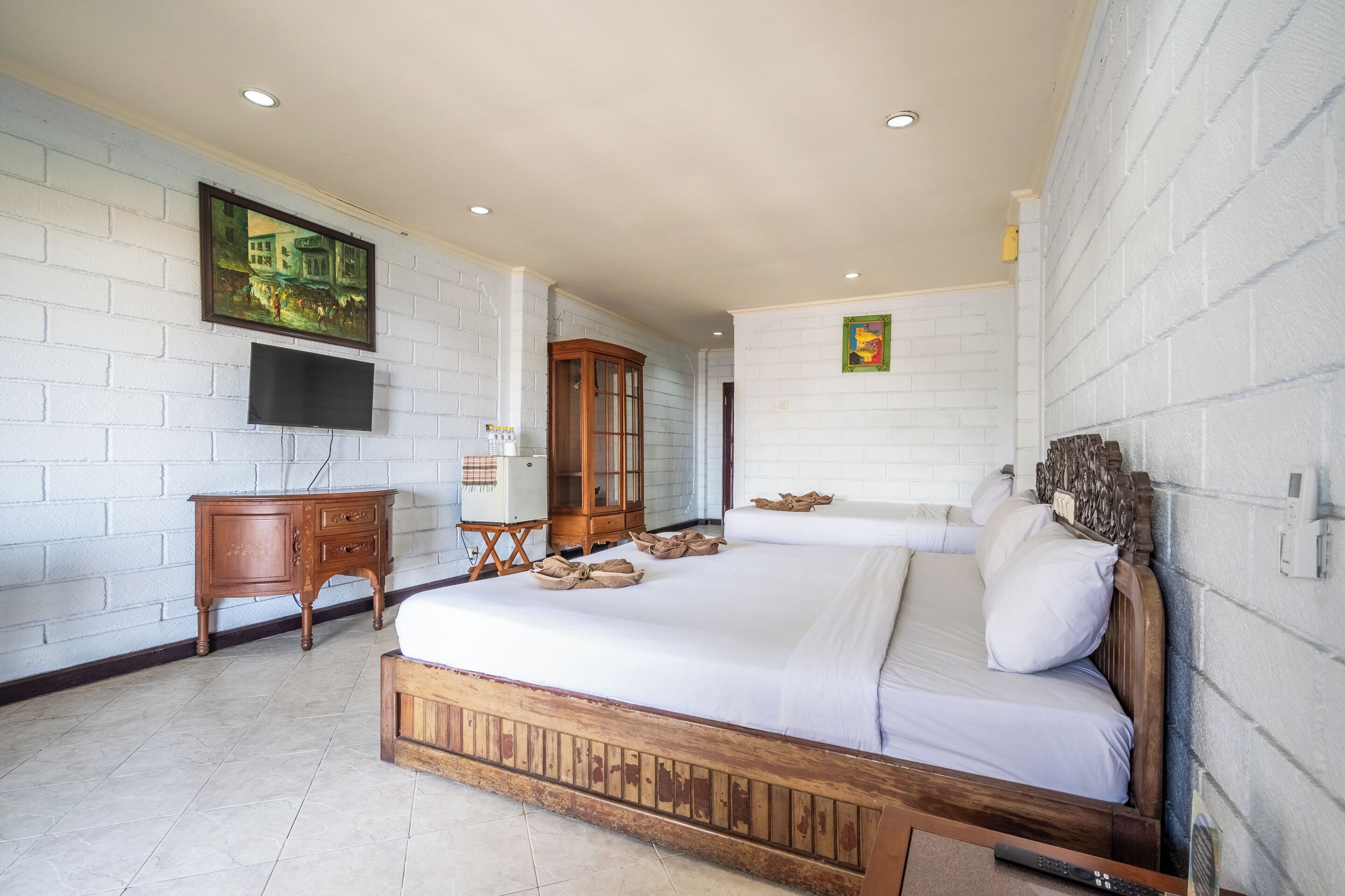 A bedroom with a wooden bed, a television mounted on the wall, a wooden cabinet, and a painting.