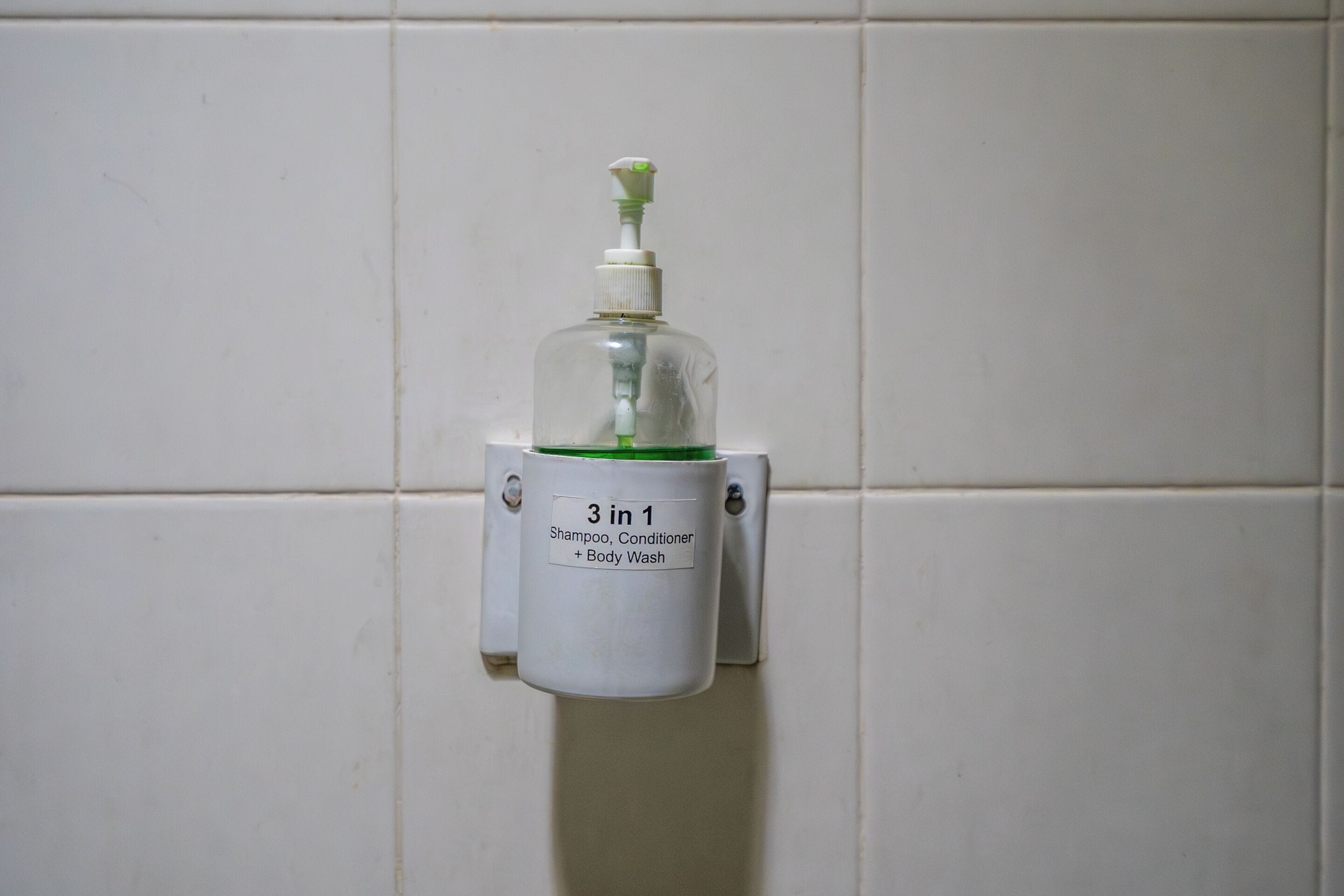 A dispenser with a label indicating it contains shampoo, conditioner, and body wash.