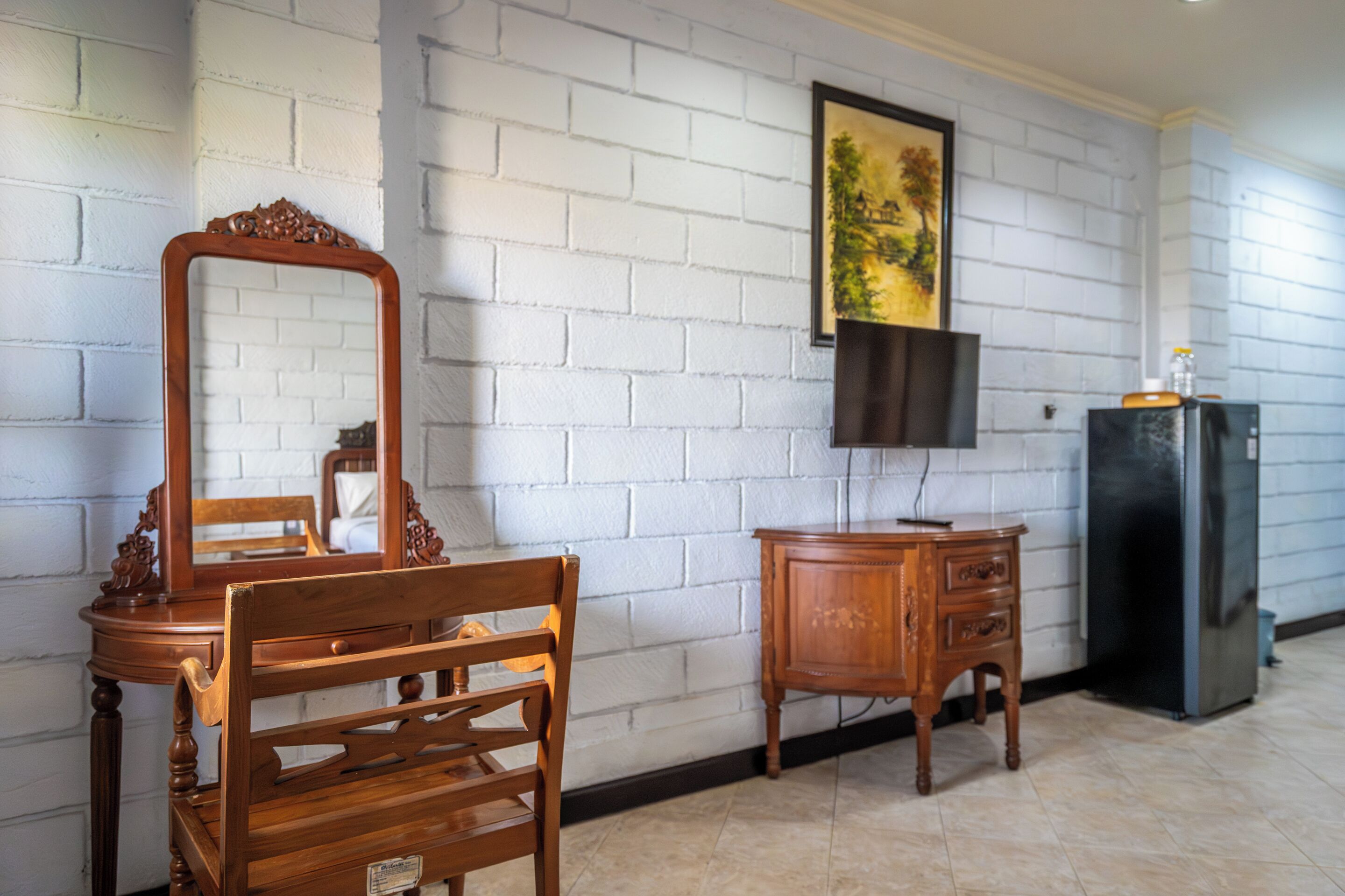Una habitación con un aparador de madera, un espejo, una silla, un televisor montado en la pared y un refrigerador.