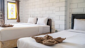 Een hotelkamer met twee bedden, witte lakens, een bakstenen muur, een raam met gordijnen en een handdoek op het bed.