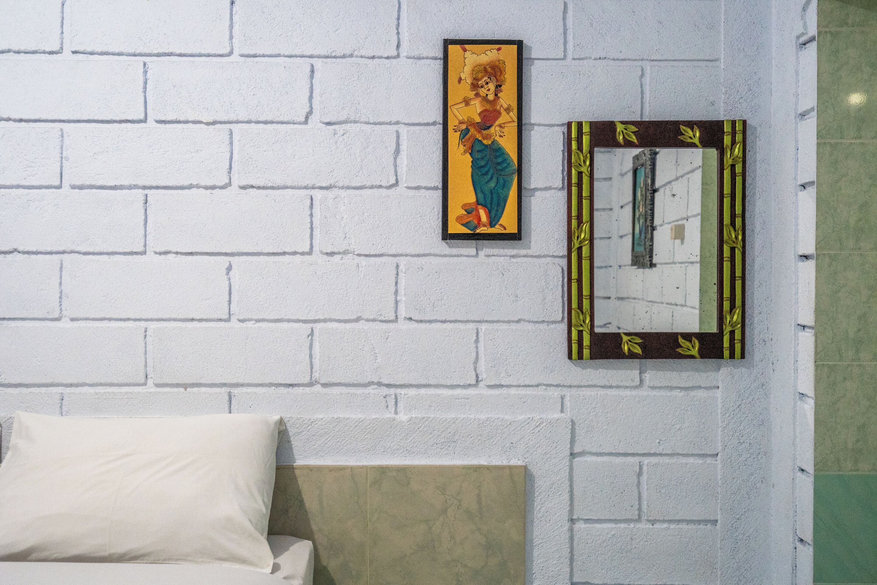 Una habitación con pared de ladrillo blanco, una cama con cabecera color beige y dos cuadros enmarcados.