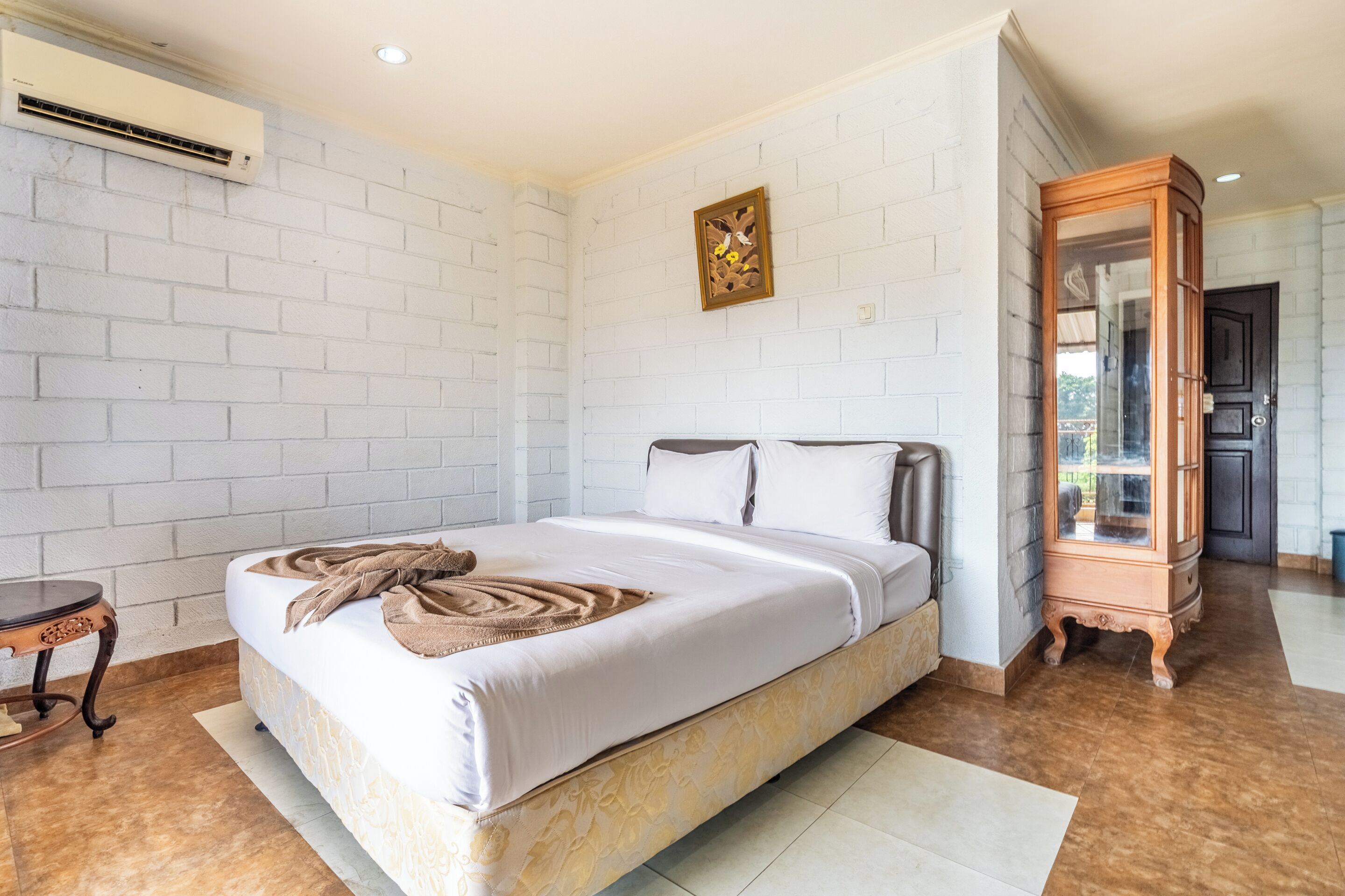 A bedroom with a bed, a wooden cabinet, and a white brick wall.