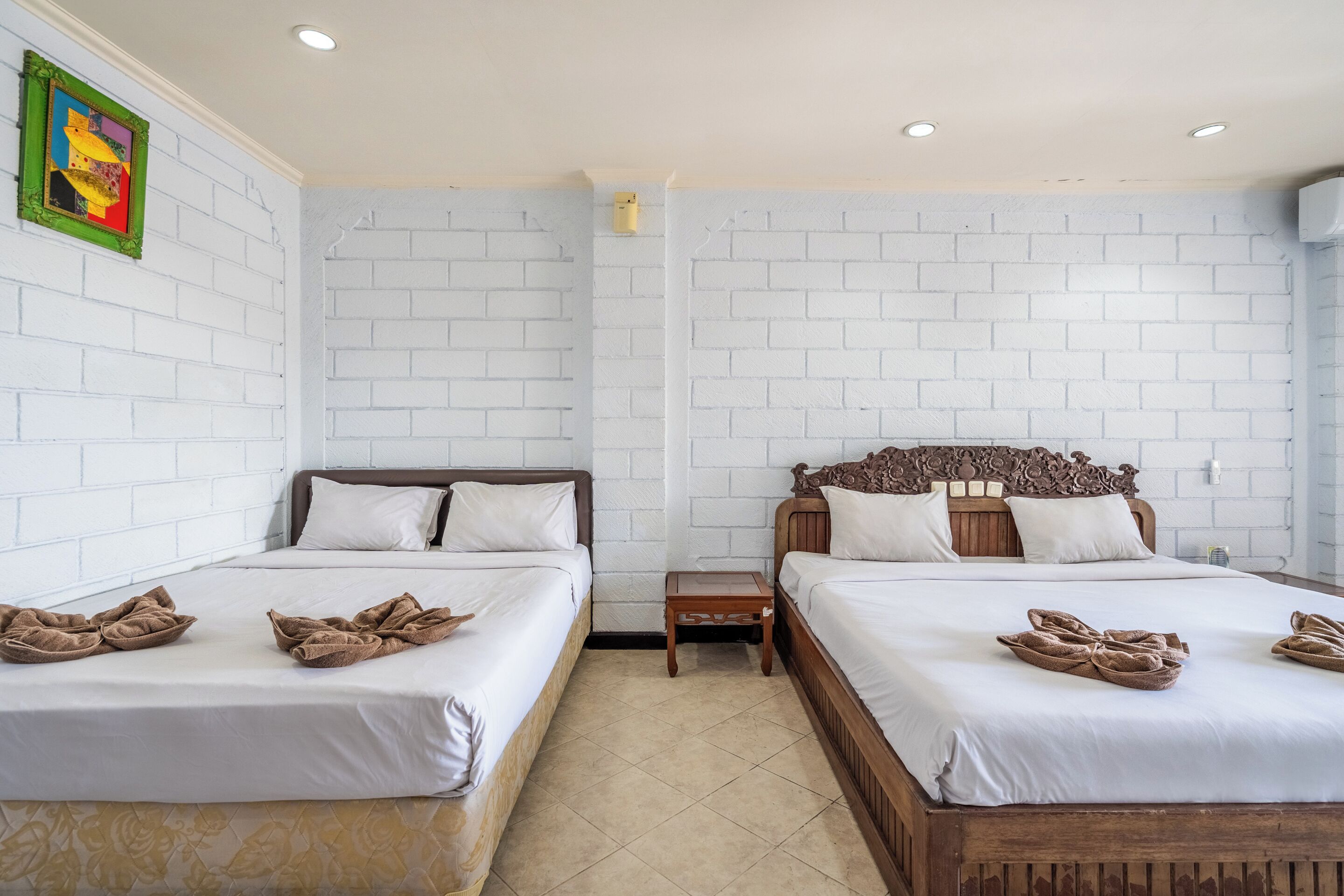 Una habitación de hotel con dos camas, paredes de ladrillo blanco y una mesita de noche de madera.