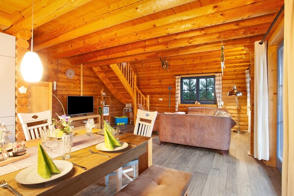 L’intérieur d’un chalet en bois comprend un coin repas, un canapé, un téléviseur et un escalier.