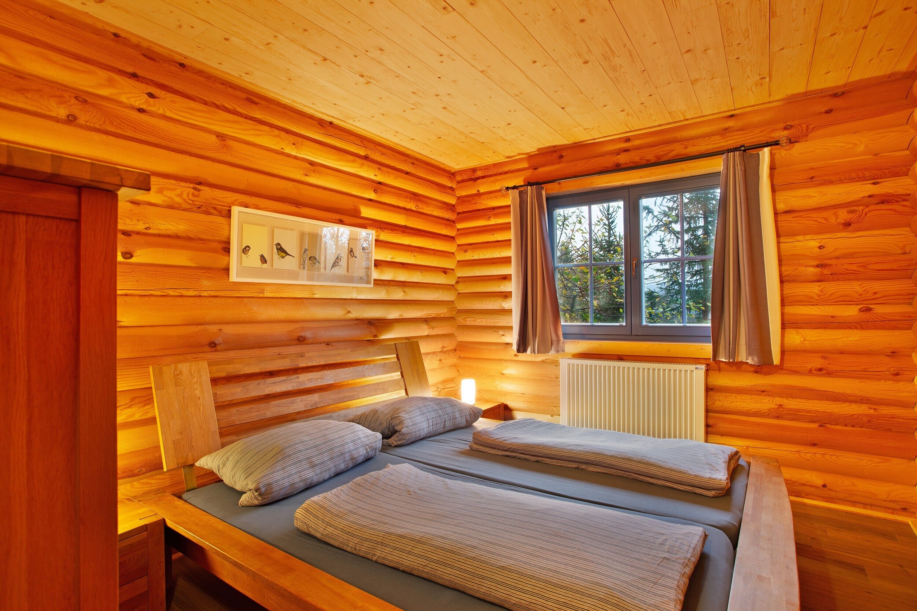 A log cabin bedroom with two beds, a window with curtains, and a framed picture on the wall.