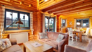 Interior de una cabaña de madera con piso de madera, un sofá, una mesa de comedor y una ventana con vistas.