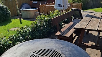 Ein Patio mit einem runden Tisch, Holzbanken und einem Whirlpool.