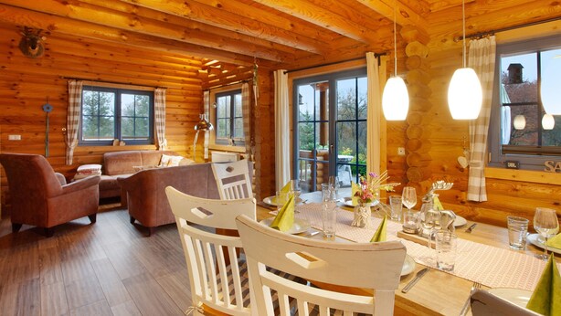 Interior de una cabaña de madera con una mesa de comedor para dos personas, un sofá y una chimenea.