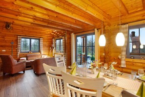 A wooden cabin interior with a dining table set for two, a sofa, and a fireplace.