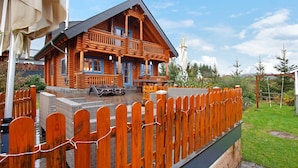 Una cabaña de troncos con un balcón, un patio con mobiliario exterior y una valla de madera.