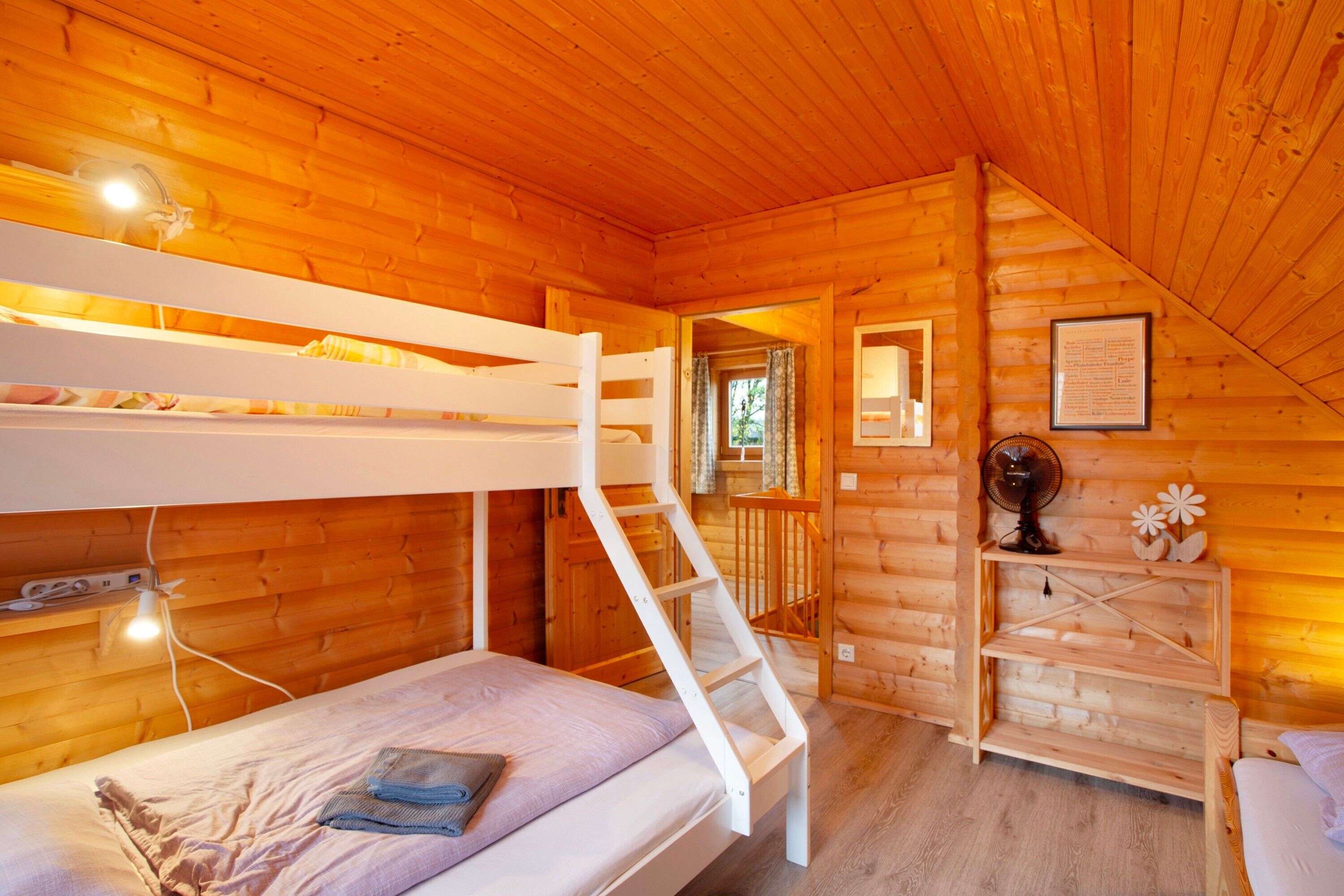 Une cabane en bois avec des lits superposés, un escalier, un ventilateur et un avis encadré accroché au mur.