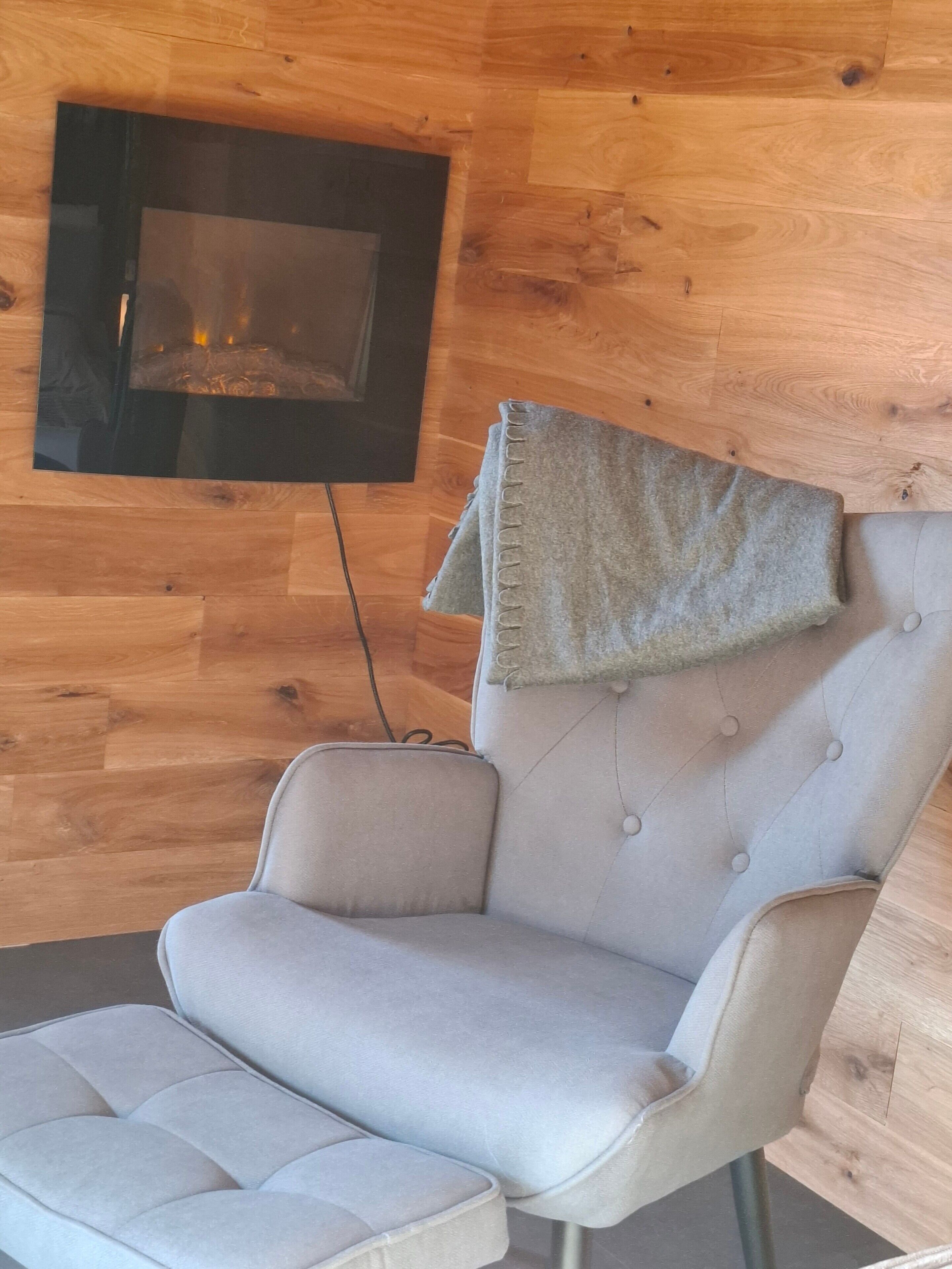 A modern room with a wooden wall, a grey upholstered armchair, and a fireplace.