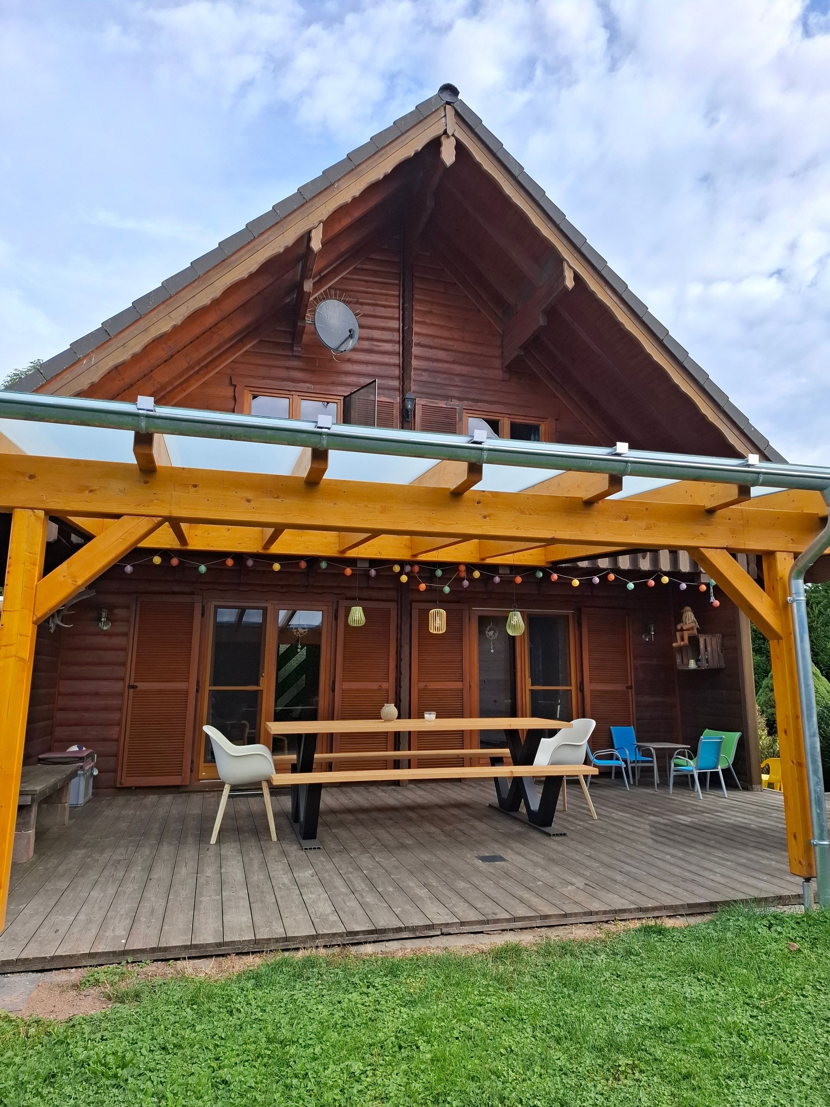 A wooden cabin with a covered deck, outdoor seating, and a satellite dish.