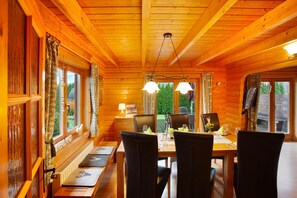 Ein Holzblockhaus-Innenraum mit Esstisch, Stühlen und einem Fenster mit Blick auf Grünflächen.