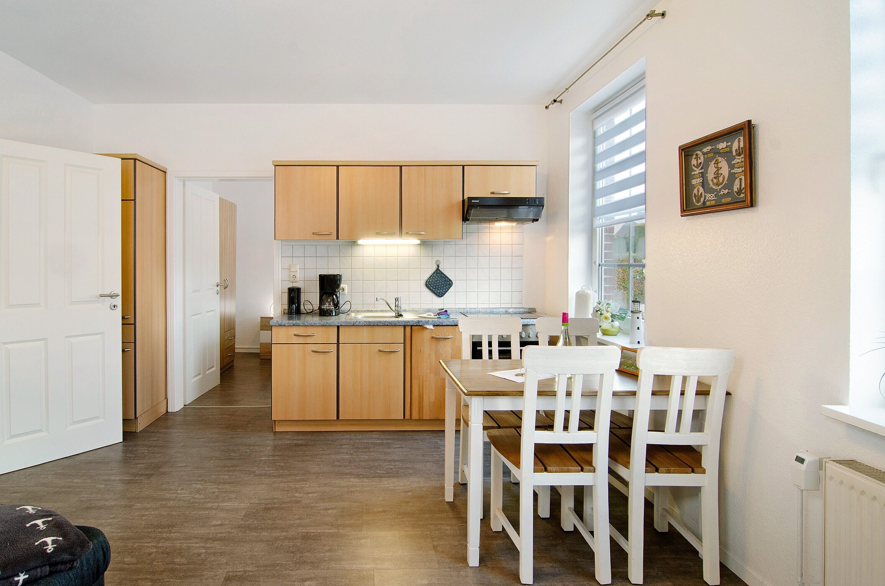 A compact kitchen with wooden cabinets, a dining table with chairs, and a window with blinds.
