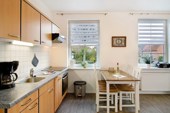 A kitchen with wooden cabinets, a sink, a stove, a window with blinds, and a dining table with chairs.