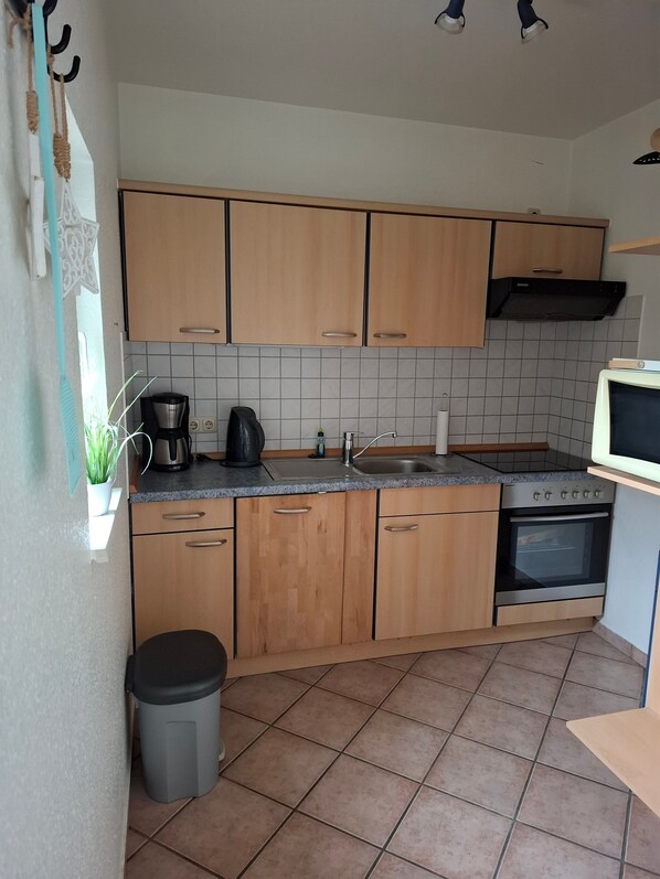 A kitchen with wooden cabinets, a sink, a stove, and a trash bin.