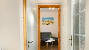 A narrow hallway with a wooden door frame, a small round table with a plant, a dark sofa, and a painting on the wall.