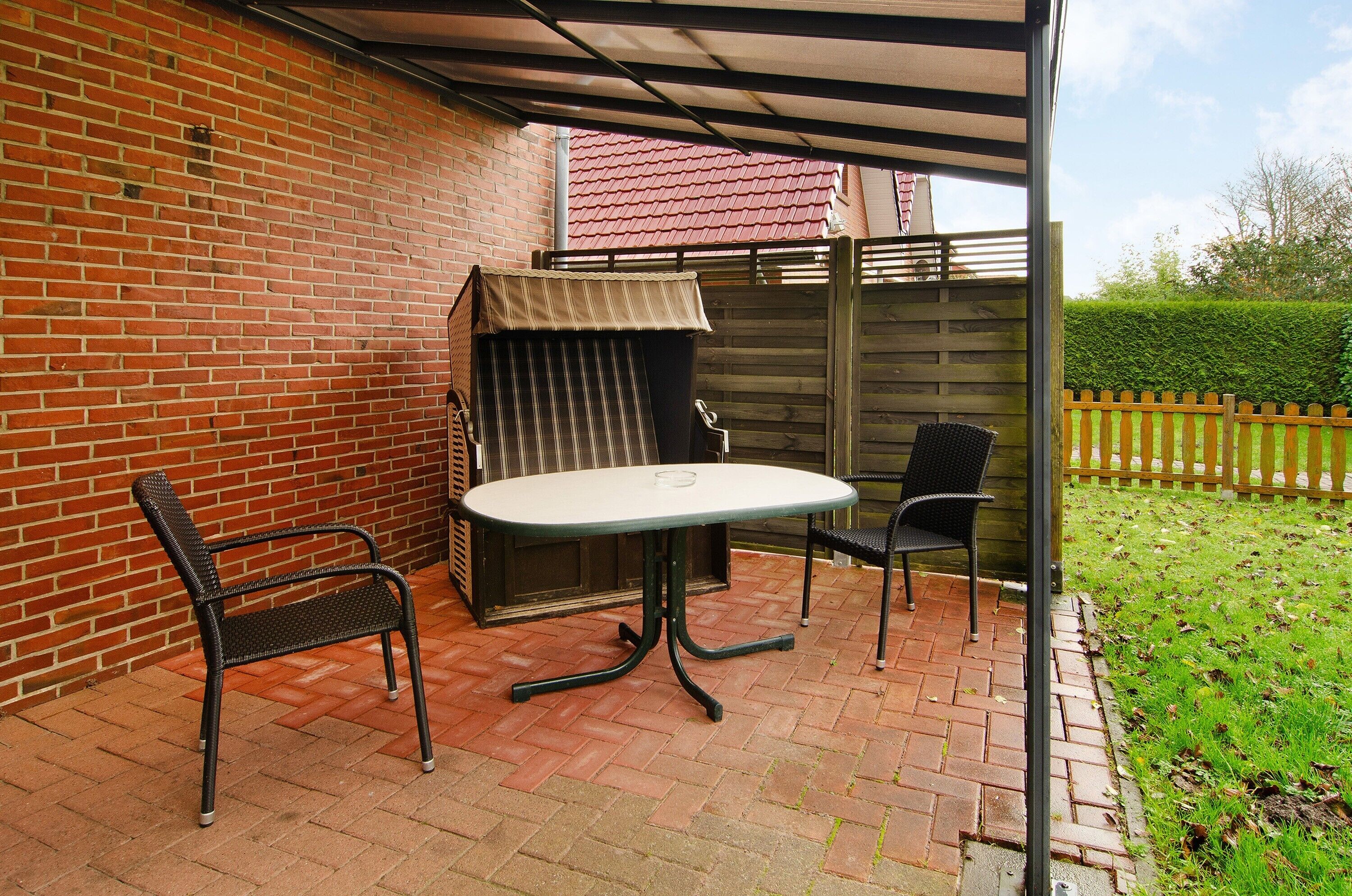 A patio with a brick floor, a table, two chairs, and a small covered seating area.