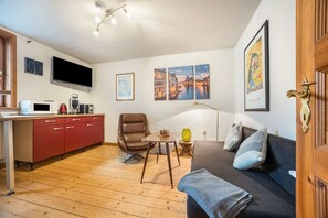 A modern living room with a sofa, a coffee table, a red kitchen unit, and a flat-screen TV mounted on the wall.