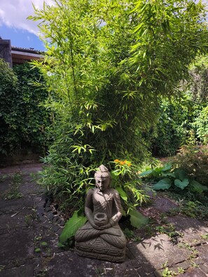 A stone Buddha statue in a garden with dense foliage and a clear sky.