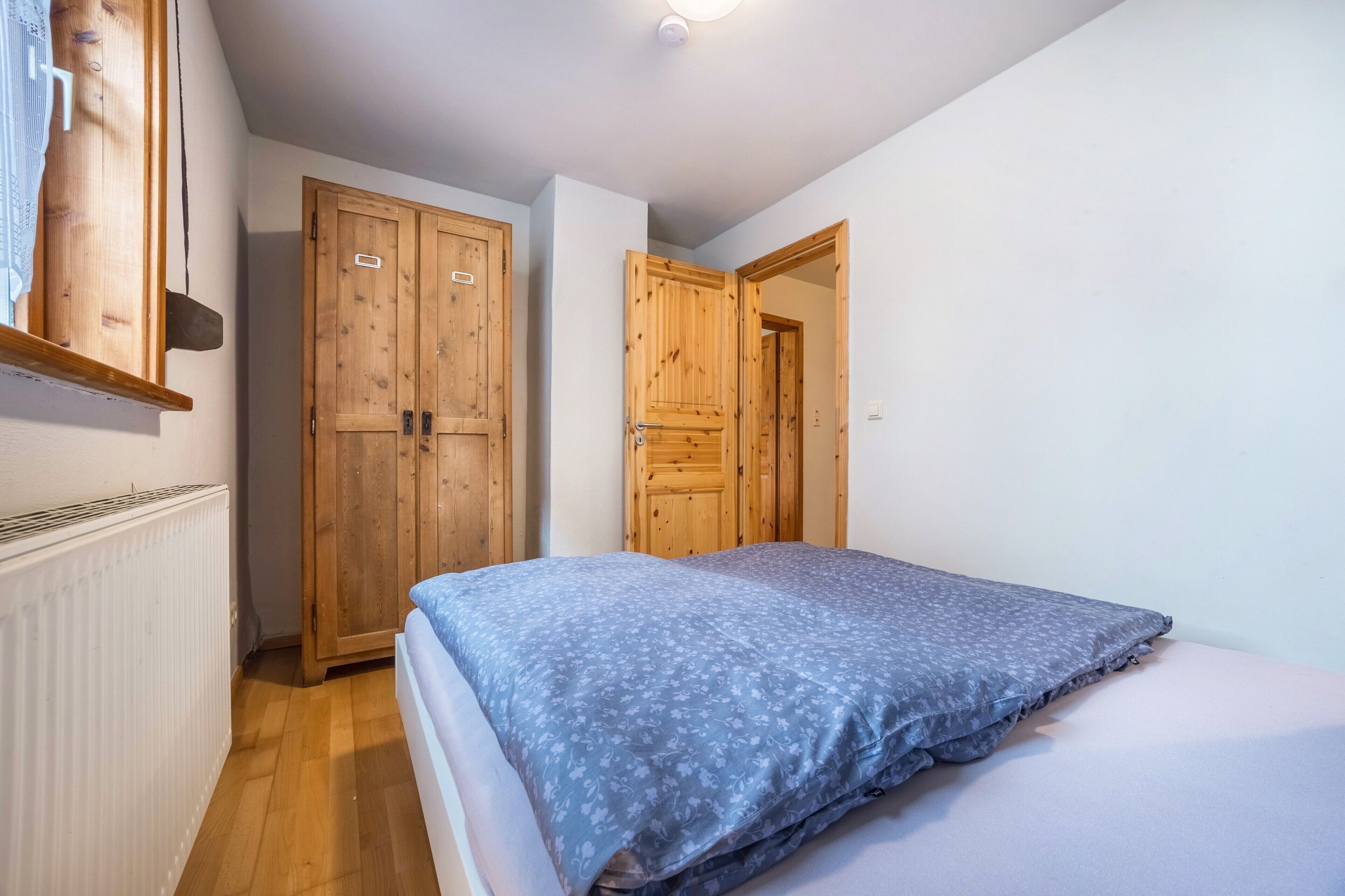 Ein Schlafzimmer mit einem Bett, einem Holzschrank und einer Tür zu einem weiteren Raum.