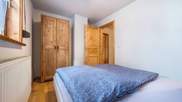 Ein Schlafzimmer mit einem Bett, einem Holzschrank und einer Tür zu einem weiteren Raum.