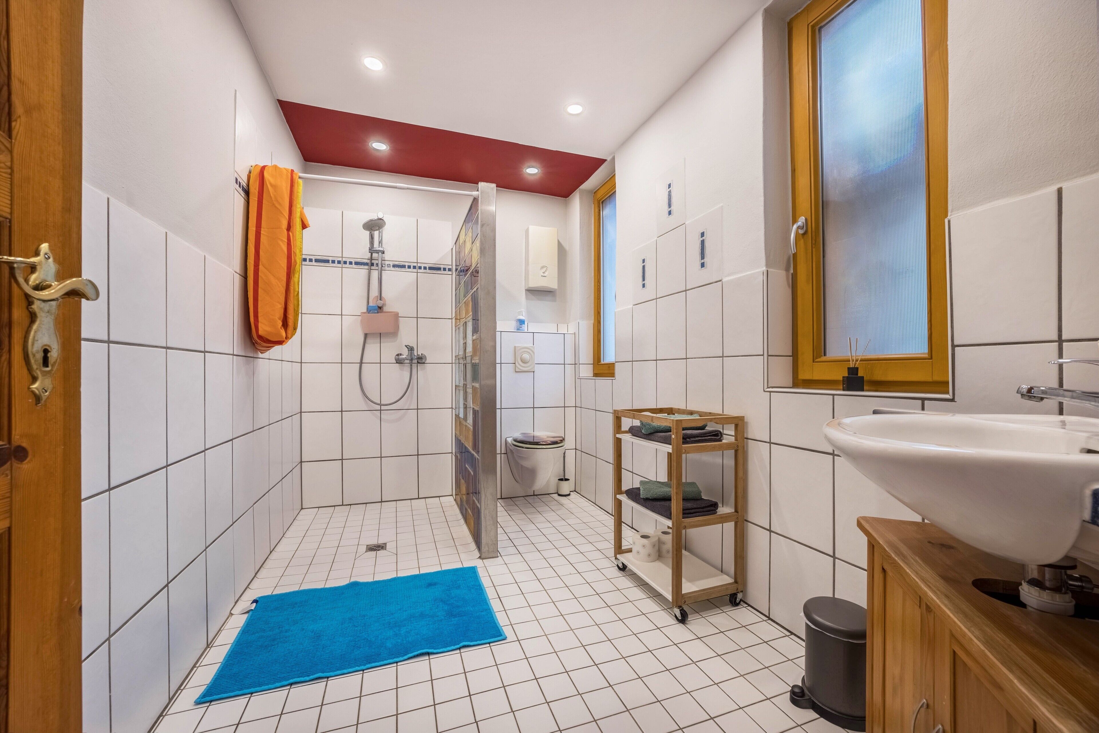 Ein Badezimmer mit weißen Fliesen, einer Dusche, einer Toilette, einem Waschbecken und einer blauen Badmatte.