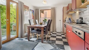 A kitchen with a checkered floor, a dining table with chairs, and a view through a glass door to an outdoor area. - Apartment 'Einzimmer Appartment' with Private Terrace and Wi-Fi (Bad Gandersheim)