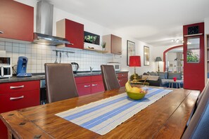 Une cuisine moderne avec des meubles de rangement rouges, une table à manger en bois et un panier de fruits.