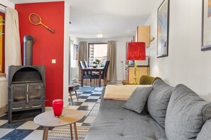 Un salon avec un canapé, une table, un mur rouge, une cheminée et, au fond, un coin repas.