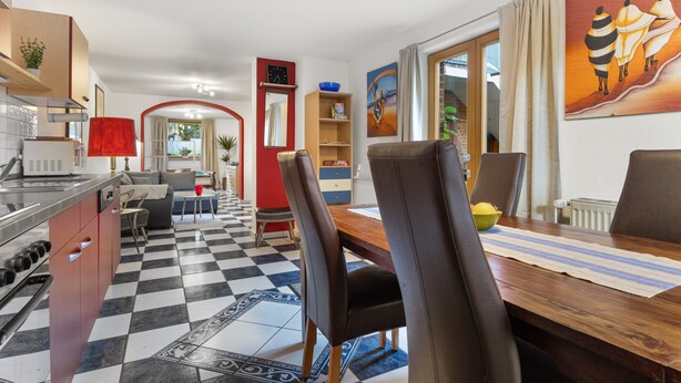 A modern kitchen with a checkered floor, a dining area with a wooden table and chairs, and a living room with a sofa and a red archway. - Apartment 'Einzimmer Appartment' with Private Terrace and Wi-Fi (Bad Gandersheim)