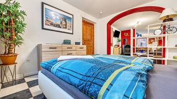 Een slaapkamer met een bed, een kamerplant, een houten dressoir, een rode boogvormige doorgang en een televisie.