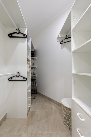 A narrow walk-through closet with white shelving, black hangers, and a tiled floor.