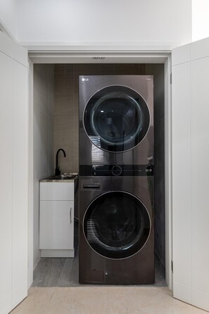 A compact laundry room with two stacked front-loading washing machines, a small sink, and a cabinet.