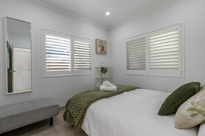A bedroom with a bed, a bench, a shelf with towels, and a painting on the wall.