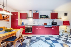 A kitchen with red cabinets, a tiled floor, and a dining area with a table and chairs.