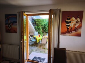 An open door leading to a balcony with a table and chairs, a radiator, and two paintings on the walls.