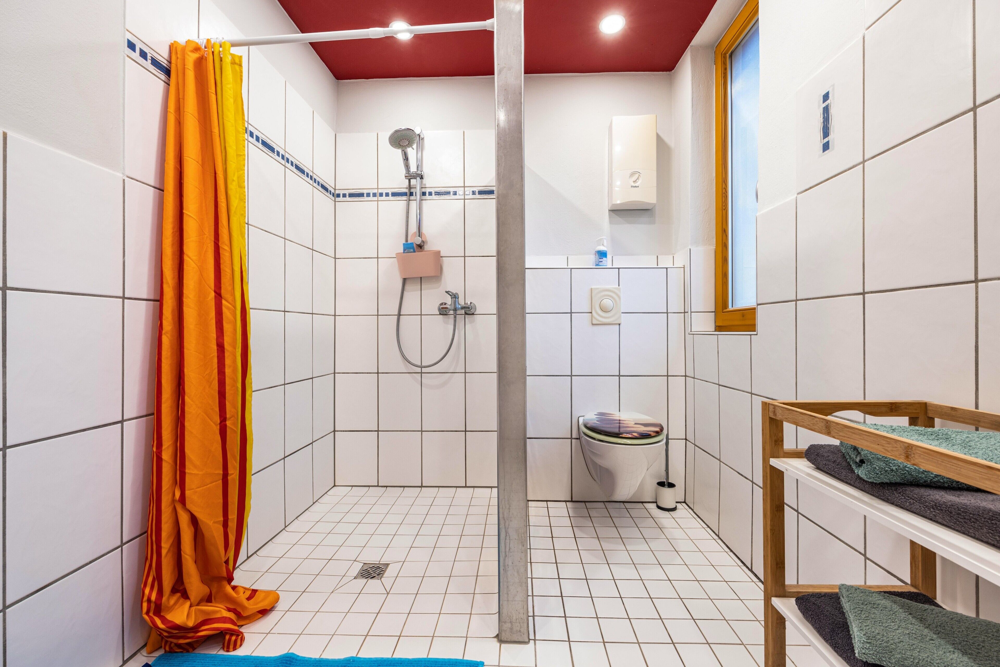 Ein kleines Badezimmer mit Fliesen, einer Dusche, einer Toilette und einem Regal mit Handtüchern.