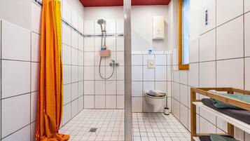 Ein kleines Badezimmer mit Fliesen, einer Dusche, einer Toilette und einem Regal mit Handtüchern.