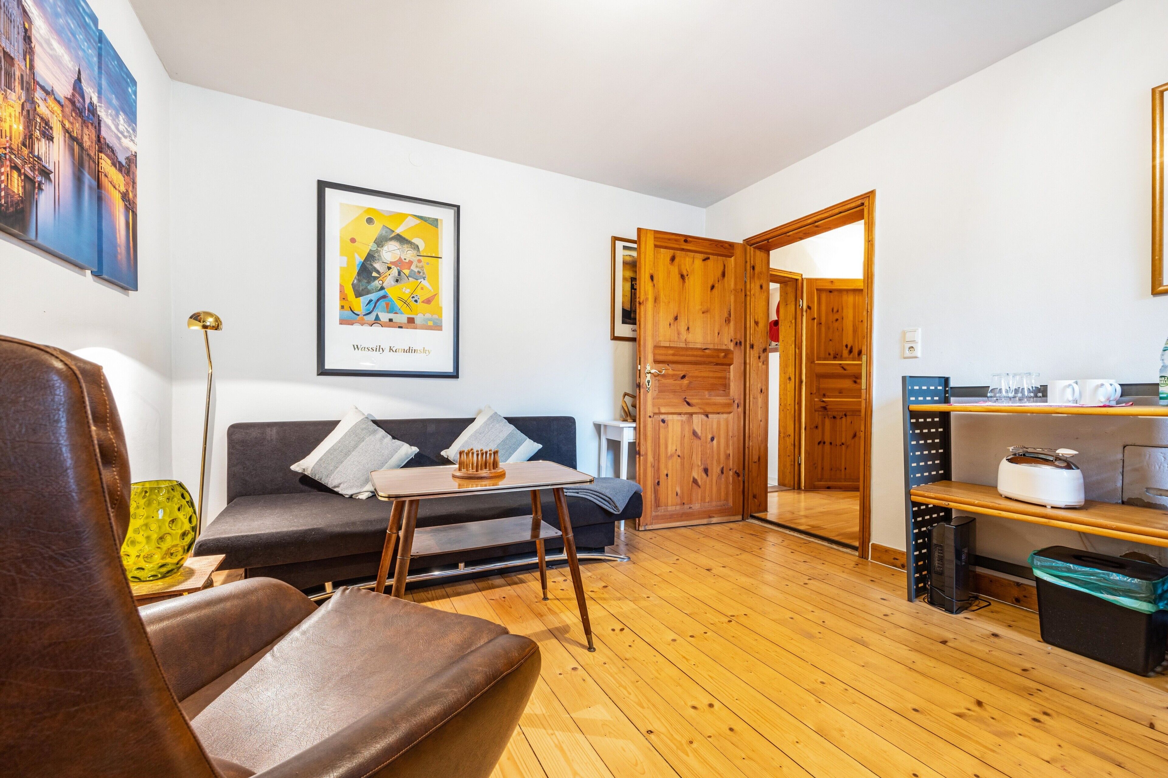 Un salon avec un canapé, une table basse et un plancher en bois. Une porte donne accès à une autre pièce.