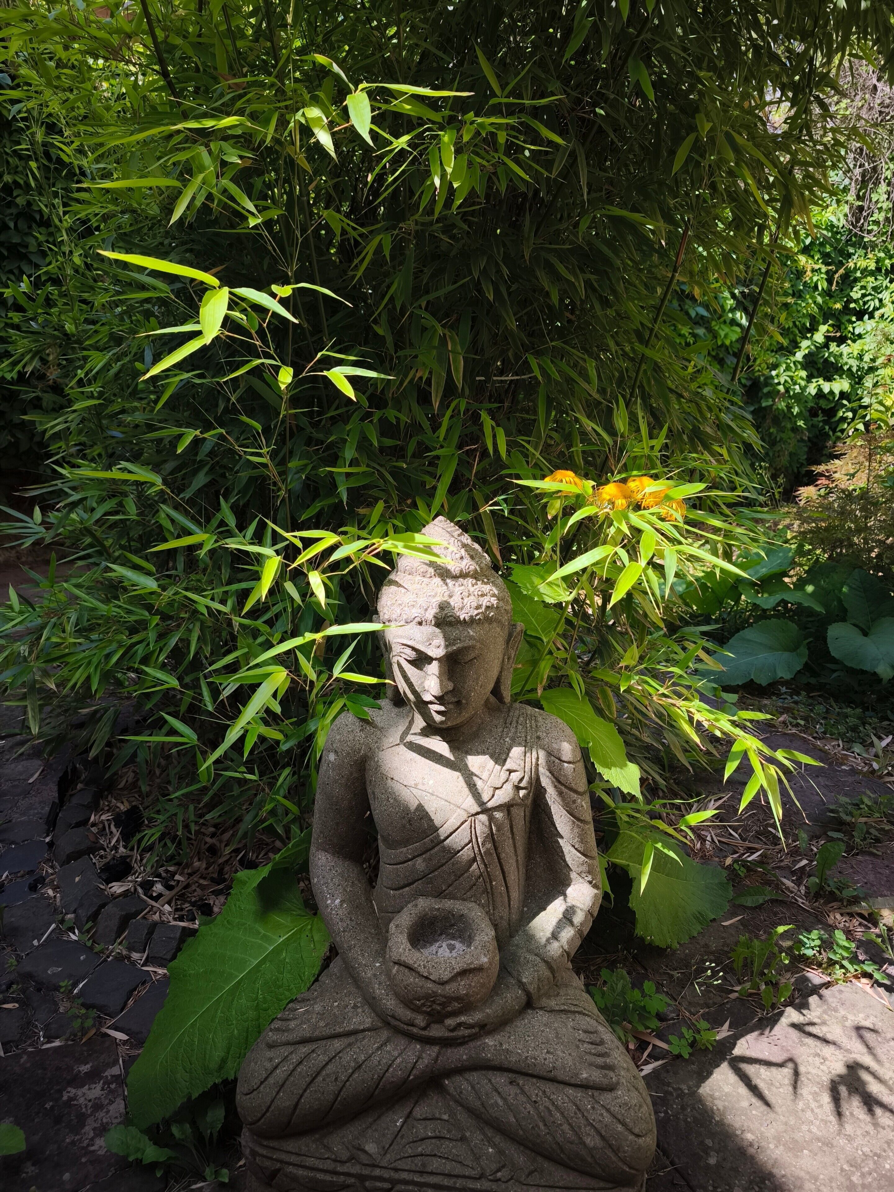 Eine Steinstatue einer sitzenden Person in einem Garten.