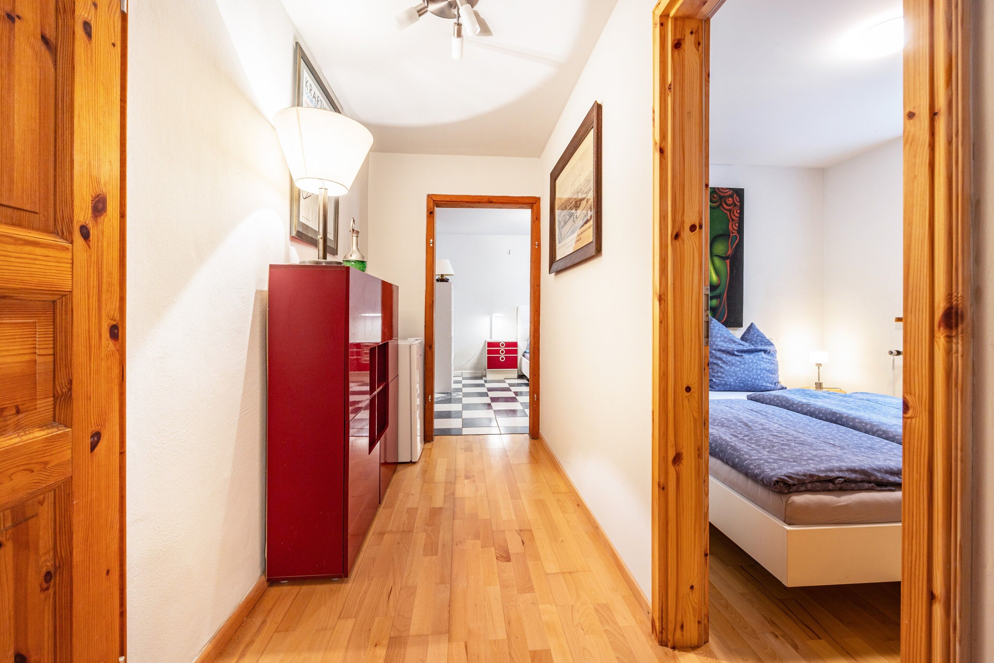 Ein schmaler Flur mit Holzboden, der zu einem Schlafzimmer mit Bett und Nachttisch führt.
