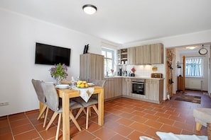 A modern kitchen with wooden cabinets, a dining table with chairs, and a flat-screen TV mounted on the wall.