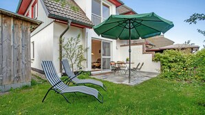 A house with a patio, two striped lounge chairs, a green umbrella, and a dining area with a table and chairs. - Holiday Home 'Schilfblick' with Lake View, Private Terrace and Wi-Fi (Wieck a Darß)