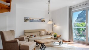 A living room with a sofa, armchair, wooden coffee table with wheels, a hanging lamp, and artwork on the wall. - Holiday Home 'Schilfblick' with Lake View, Private Terrace and Wi-Fi (Wieck a Darß)